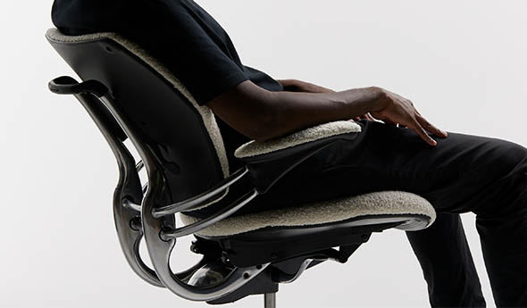 A side view of a person reclining in a black Humanscale Freedom Ocean task chair without a headrest, showcasing the weight-sensitive recline mechanism and lumbar support against a white background