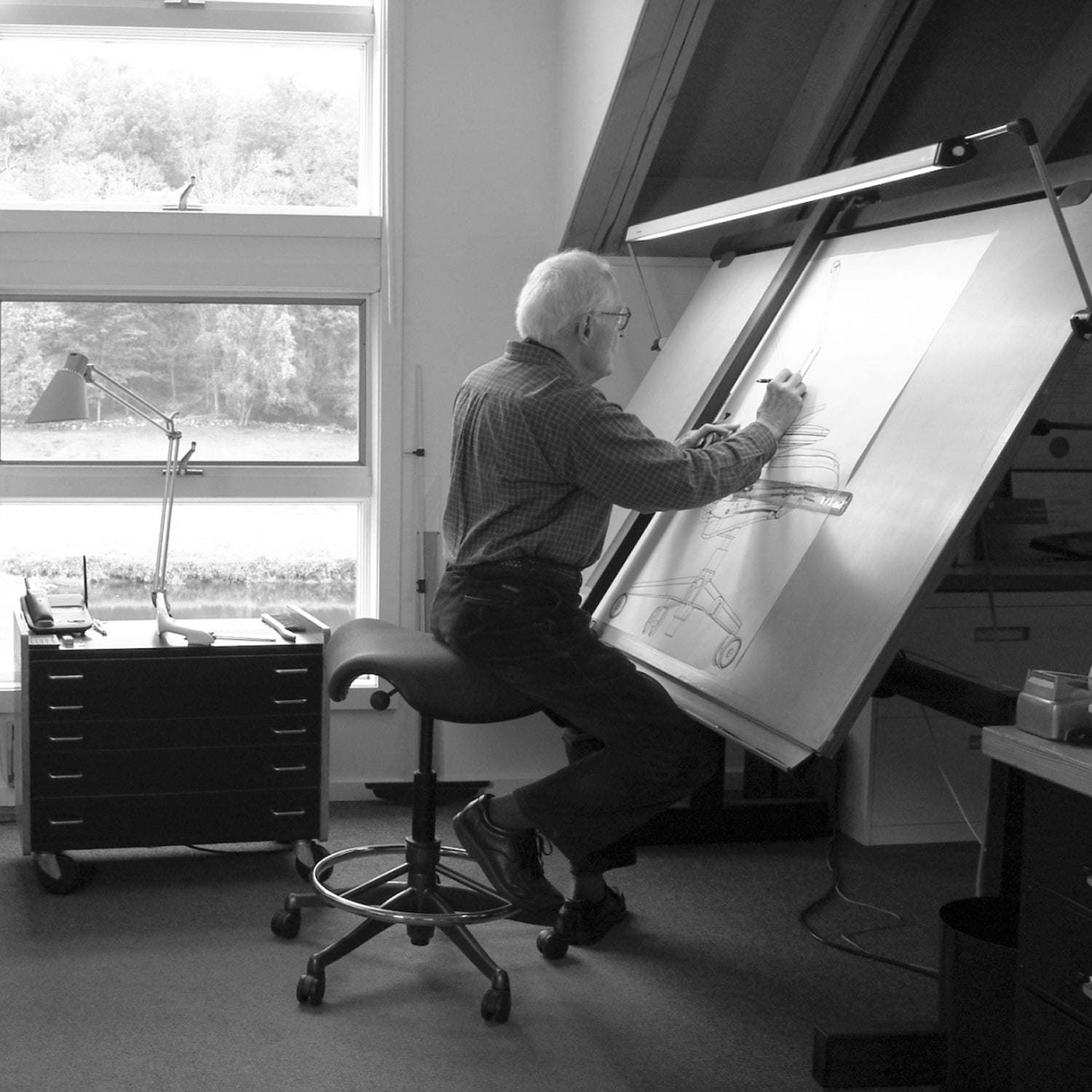 Niels Diffrient designing on board while sitting on Humanscale Freedom Saddle Stool ring base