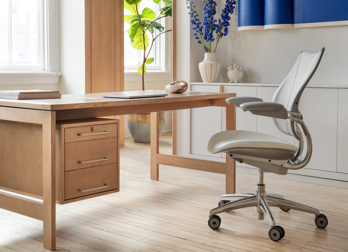 Diagonal side profile of a Humanscale Liberty Task chair with silver pinstripe mesh and a white and gray frame, showcasing its automatic lumbar support in a modern home office