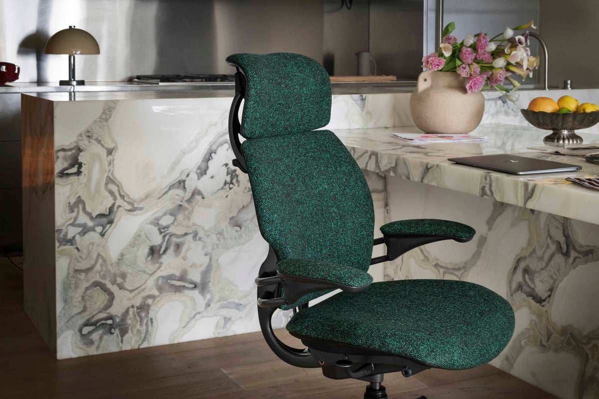 Green fabric Humanscale Freedom Ocean Headrest chair with a black frame, placed next to a luxury marble desk with a laptop and decor