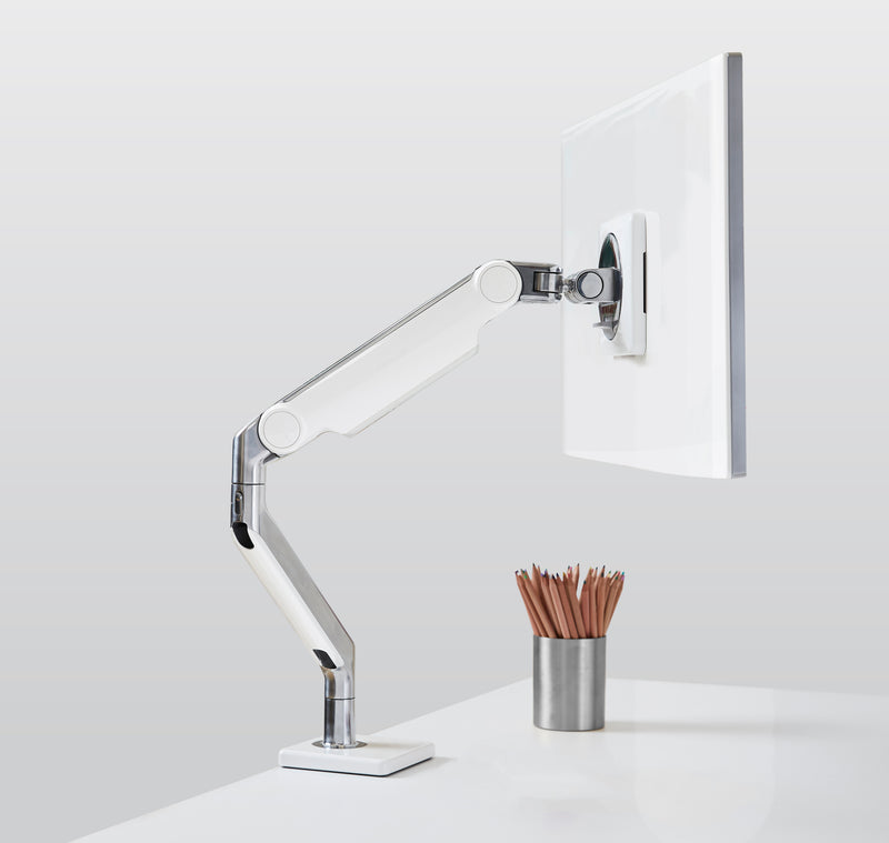 A white and polished aluminum Humanscale M2 Pro single monitor arm supporting a monitor on a white desk, with a desk clamp mount and a metal pencil holder nearby